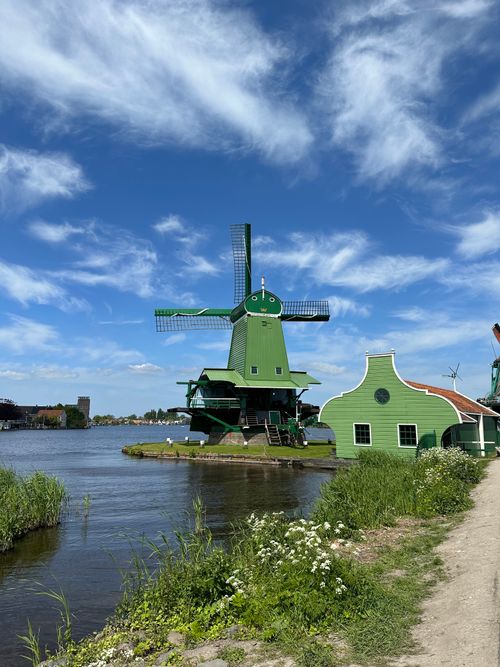 Free Beautiful green windmill by a river at Zaanse Schans, showcasing Dutch architecture under blue skies. Stock Photo