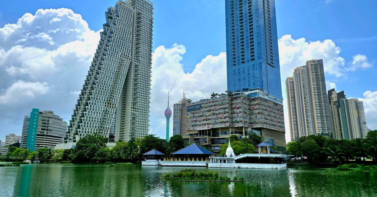 A view of Colombo's skyline with high-rise towers reflecting in a serene lake.