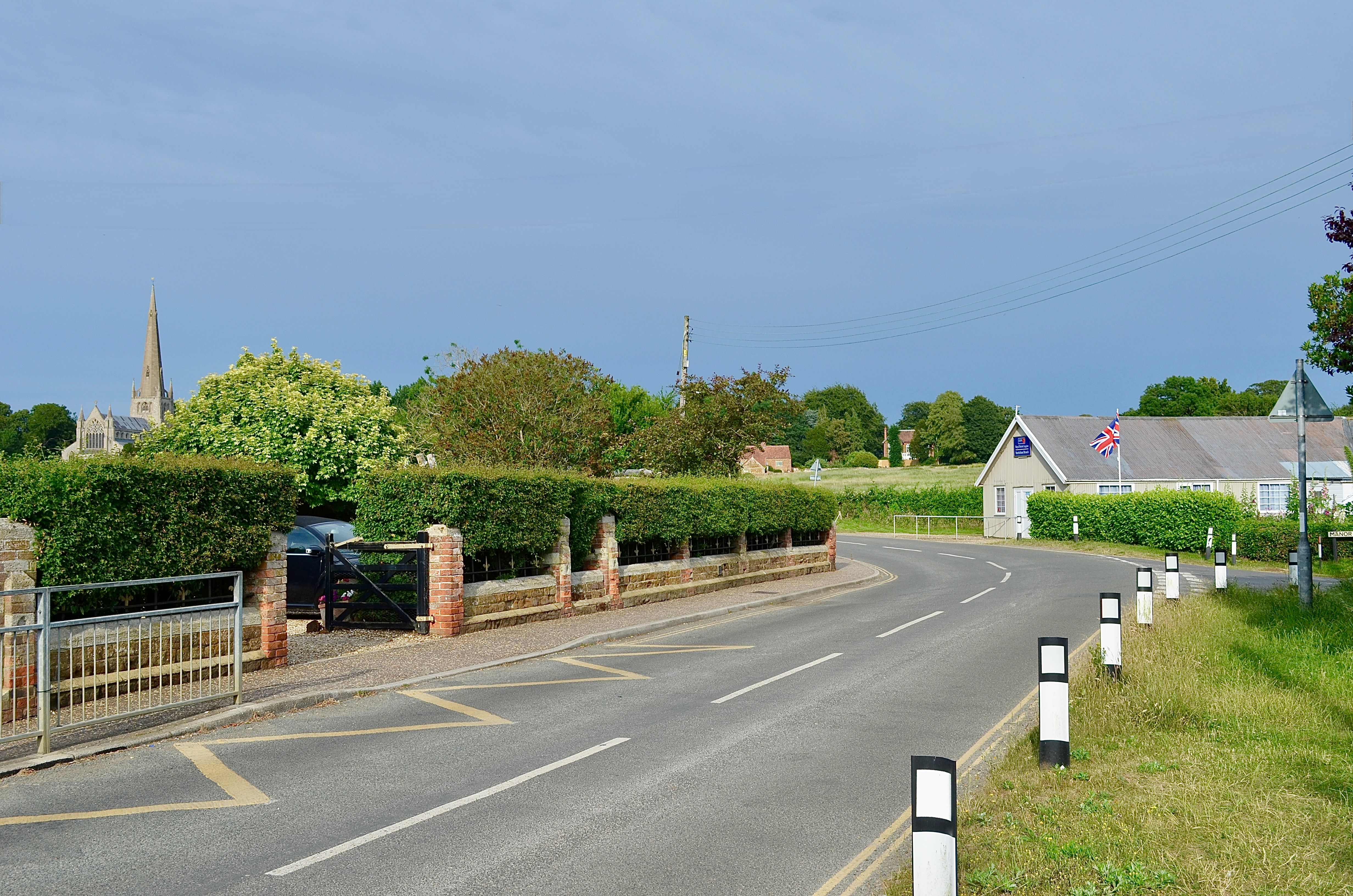 Picturesque rural road with charming village and church spire in summer scenery.