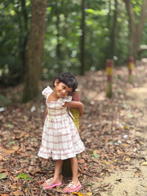 Free A young girl in a plaid dress playfully poses in a vibrant forest trail on a sunny day. Stock Photo