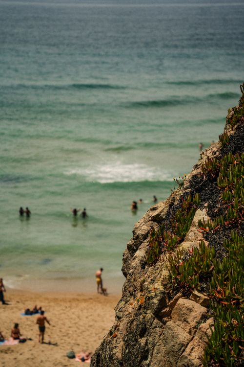 Free Scenic view of a beach with people enjoying the water, beside a rocky cliff. Stock Photo