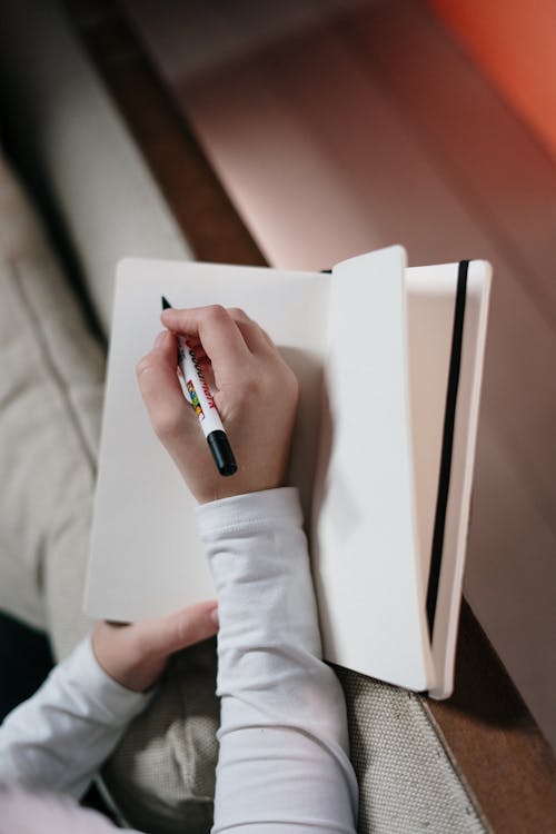 Pessoa Em Camisa Branca De Manga Comprida Segurando Caneta E Caderno