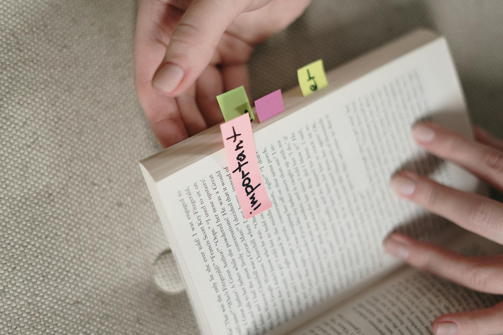 Hands holding a book with colorful sticky notes marking important pages.