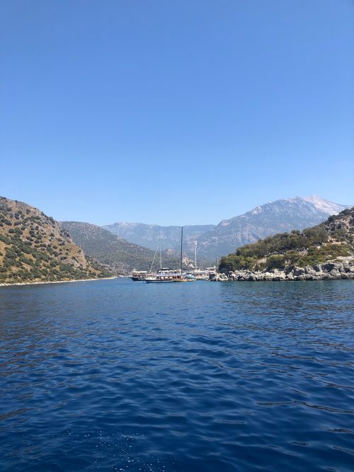 Free A peaceful sailboat drifting on a calm sea surrounded by rugged mountains and a clear sky. Stock Photo