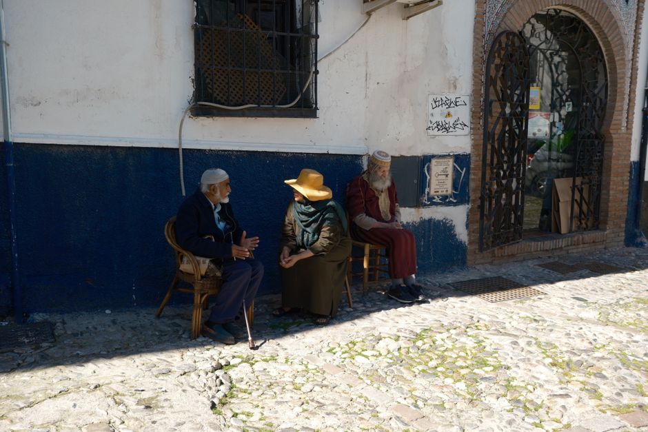 Personas mayores participan en una conversación en una esquina soleada de España.