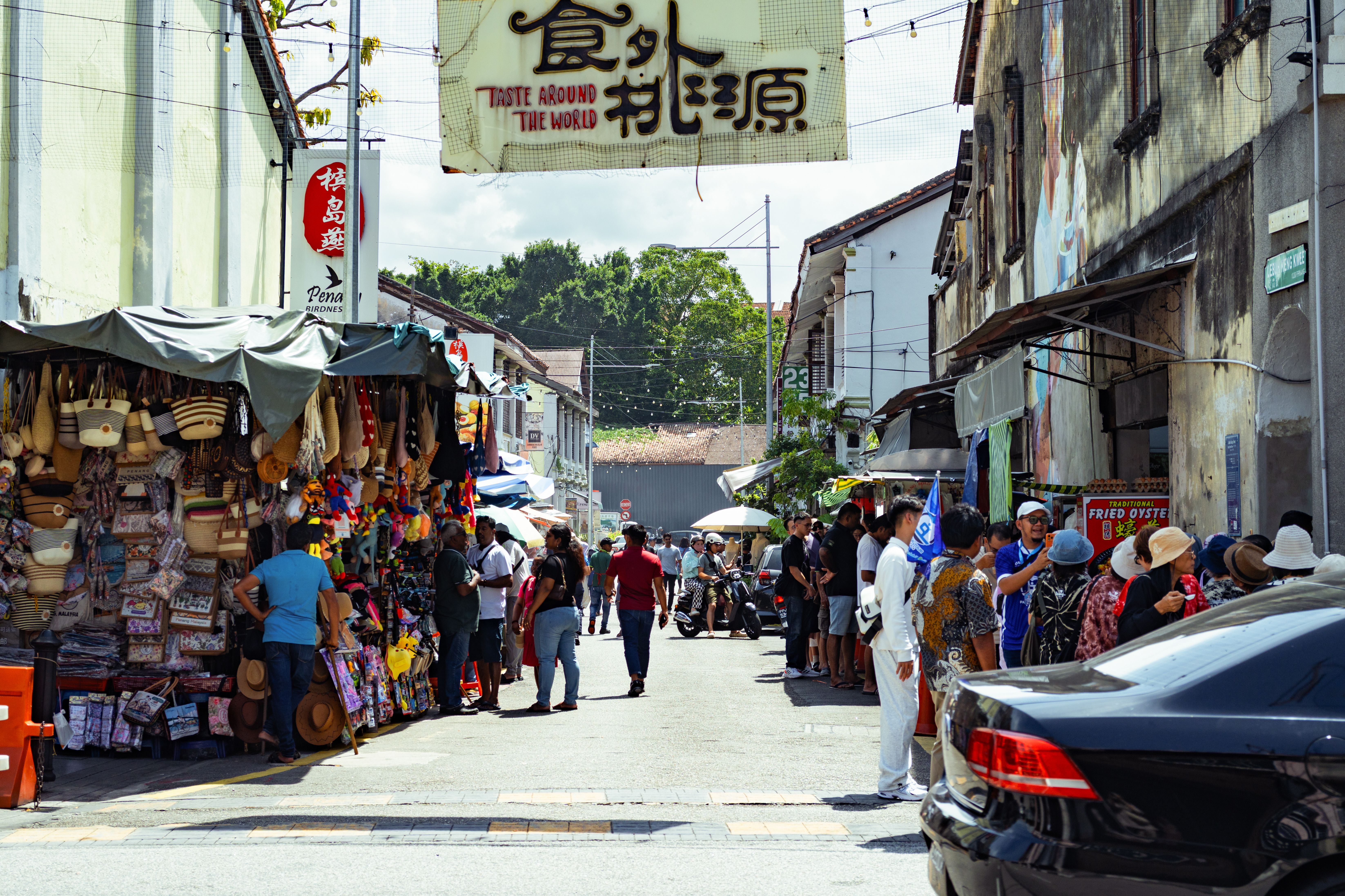 Colorful street market in George Town, Penang, bustling with locals and tourists under a bright sky.