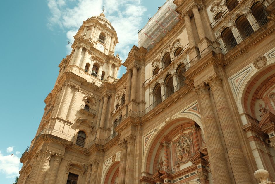 Una espectacular toma desde un ángulo ascendente capta la detallada arquitectura de la Catedral de Málaga contra un cielo azul brillante.