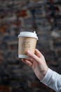 一只手握着外卖咖啡杯的特写，上面写着“是”，背景是模糊的砖墙