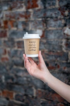 特写镜头中，手持咖啡杯置于质朴的砖墙前，传递出平静的气息