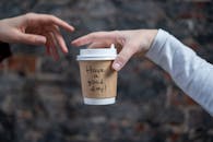 特写镜头中，一只一次性咖啡杯在两只手之间传递，上面写着“祝你有美好的一天！”