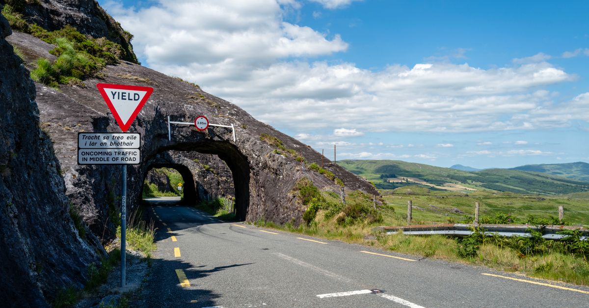 Beautiful summer view of a winding road through a rock tunnel in County Cork, Ireland.