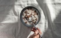 特写：一只手握着一把勺子，伸进一碗字母麦片和牛奶中