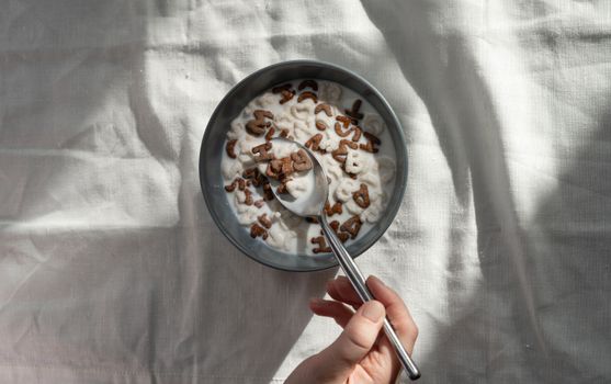 特写：一只手握着一把勺子，伸进一碗字母麦片和牛奶中