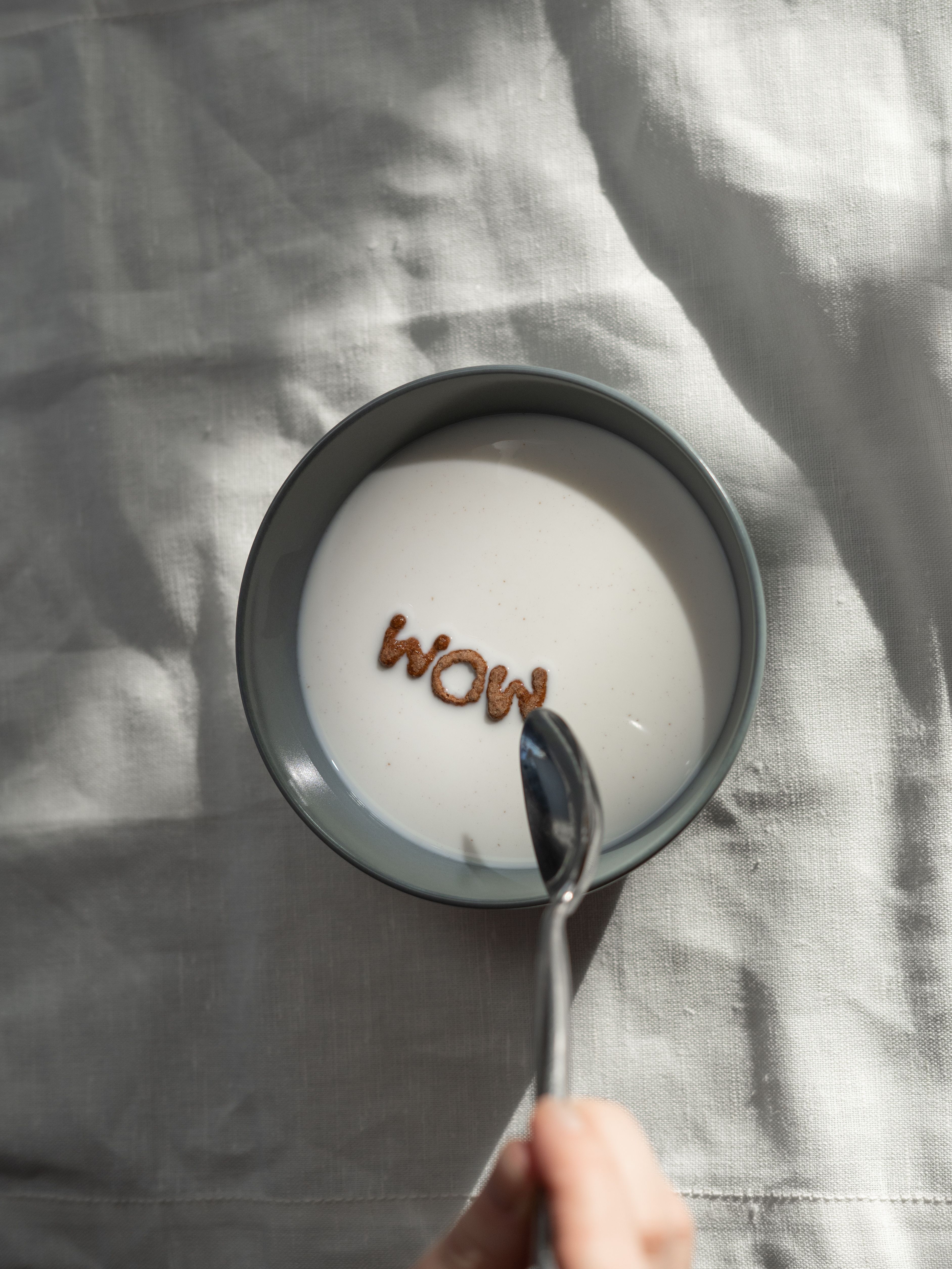 A bowl of milk with cereal letters spelling WOW held by a hand, captured from above.