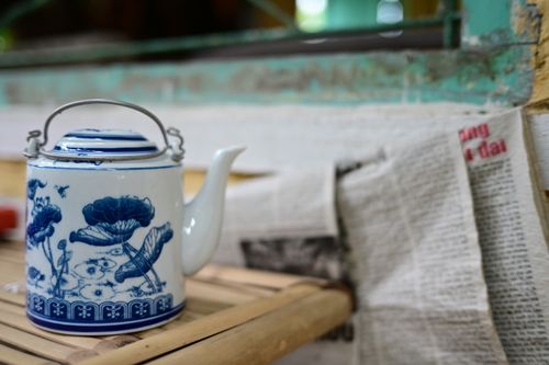 Free A close-up of a white ceramic teapot with intricate blue floral patterns, placed on a bamboo surface. Stock Photo