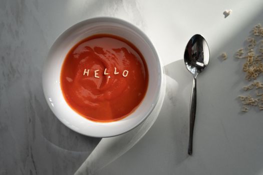 Top-down view of tomato soup with alphabet pasta spelling 'HELLO', creating a unique culinary message.