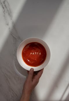 A delicious and creamy tomato soup with 'PASTA' text on top, presented on a marble surface, perfect for food enthusiasts.