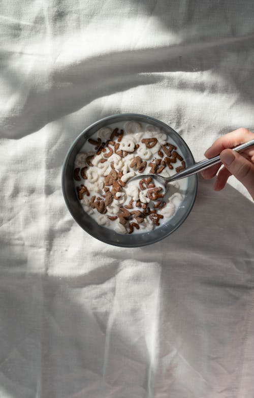 Person Holding Stainless Steel Spoon on Black Ceramic Bowl