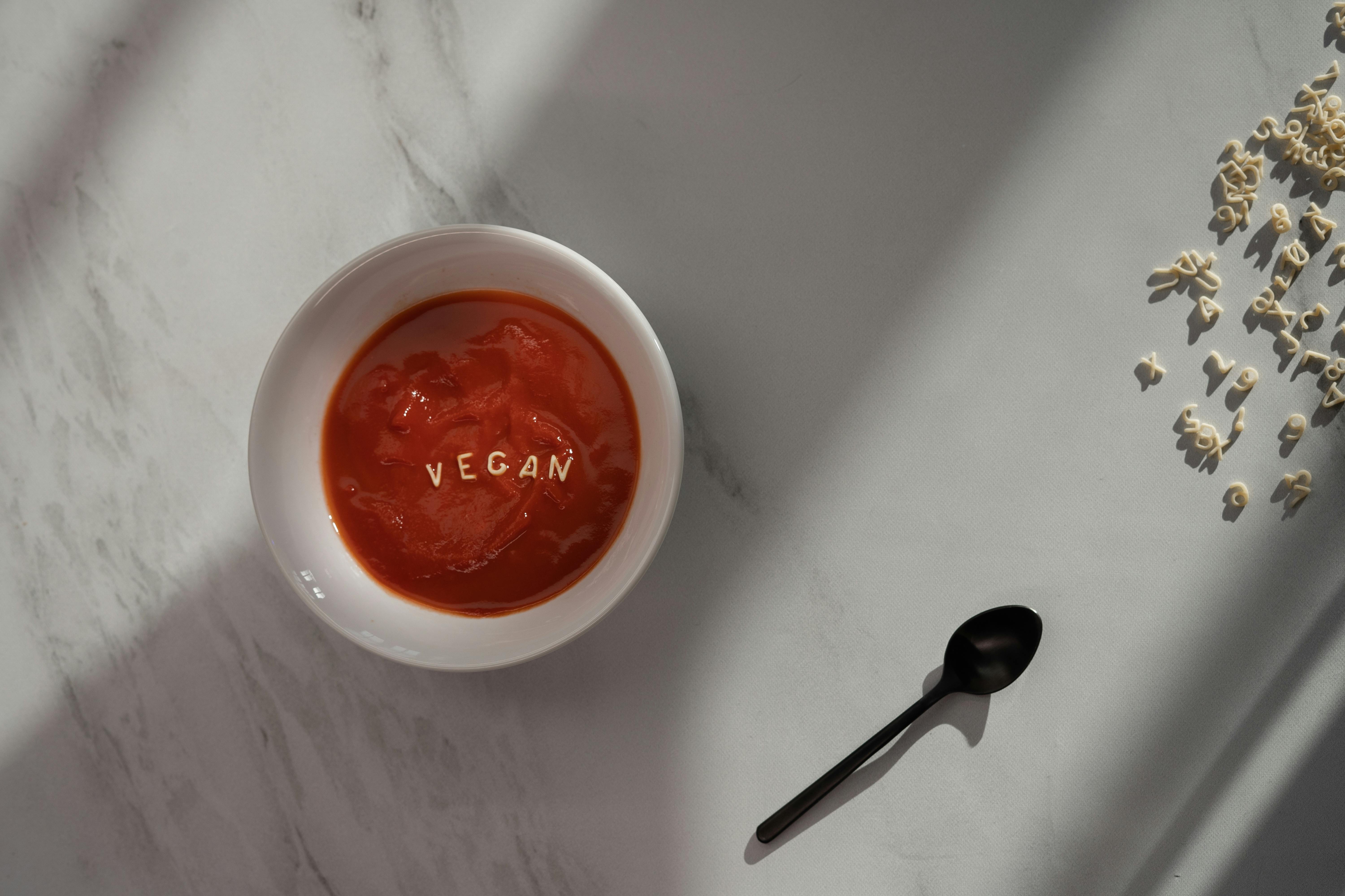 一碗素食番茄汤，配有意面字母，放在大理石表面，沐浴在自然阳光下