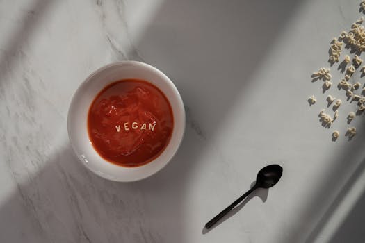 一碗素食番茄汤，配有意面字母，放在大理石表面，沐浴在自然阳光下