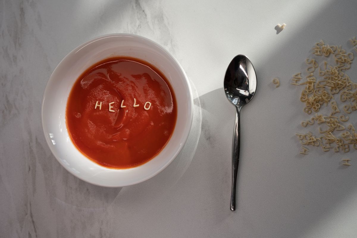 A bowl of tomato soup with alphabet pasta spelling the word HELLO, with loose pasta letters beside it