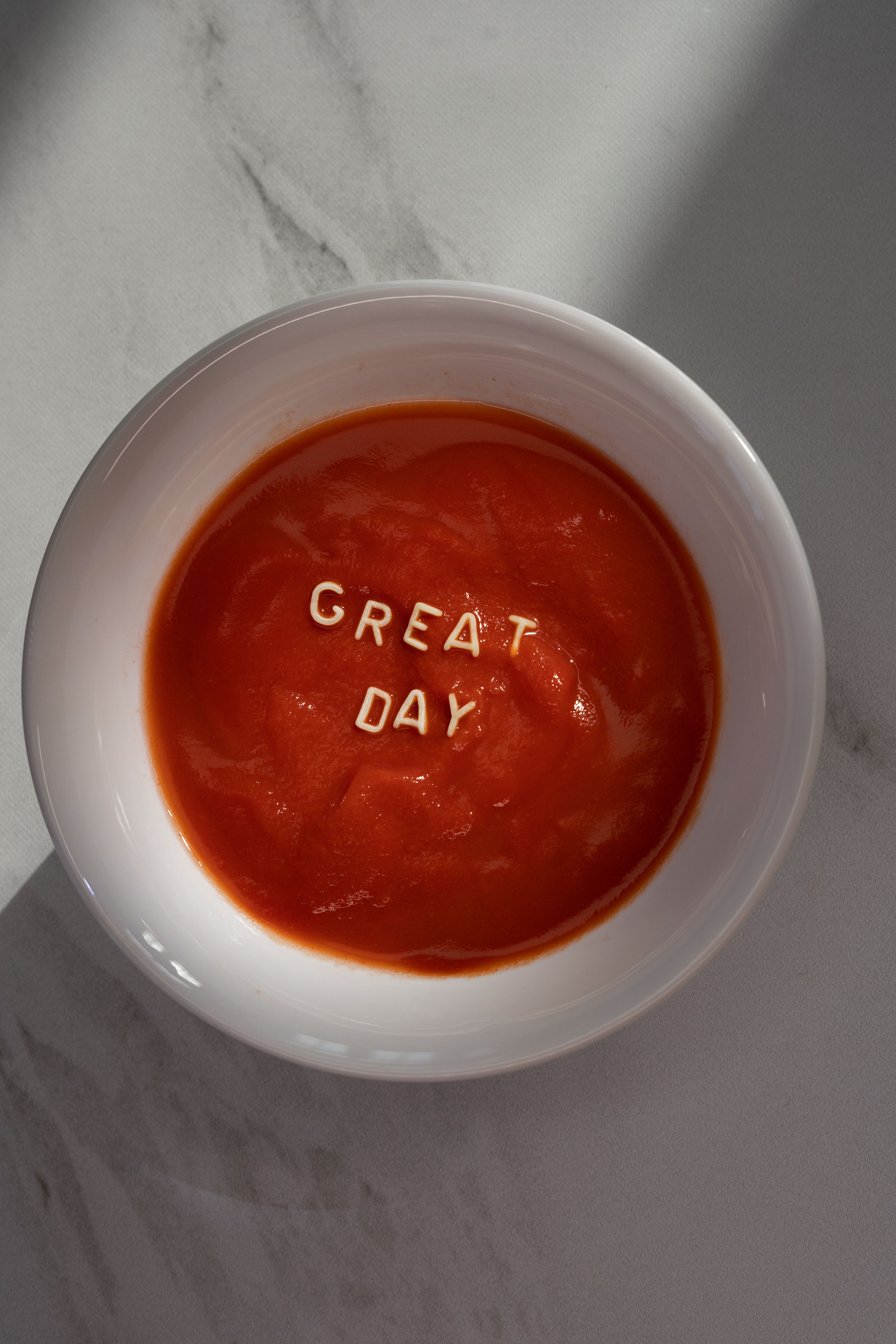 A flatlay of tomato soup with 'GREAT DAY' text on a marble surface.