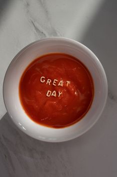 A flatlay of tomato soup with 'GREAT DAY' text on a marble surface.