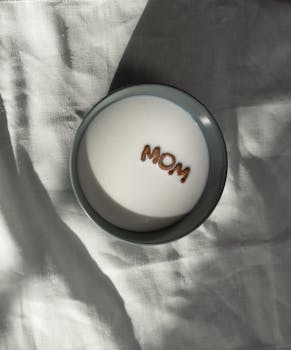 白色织物背景上，一碗牛奶与谷物拼出“妈妈”字样，顶视图