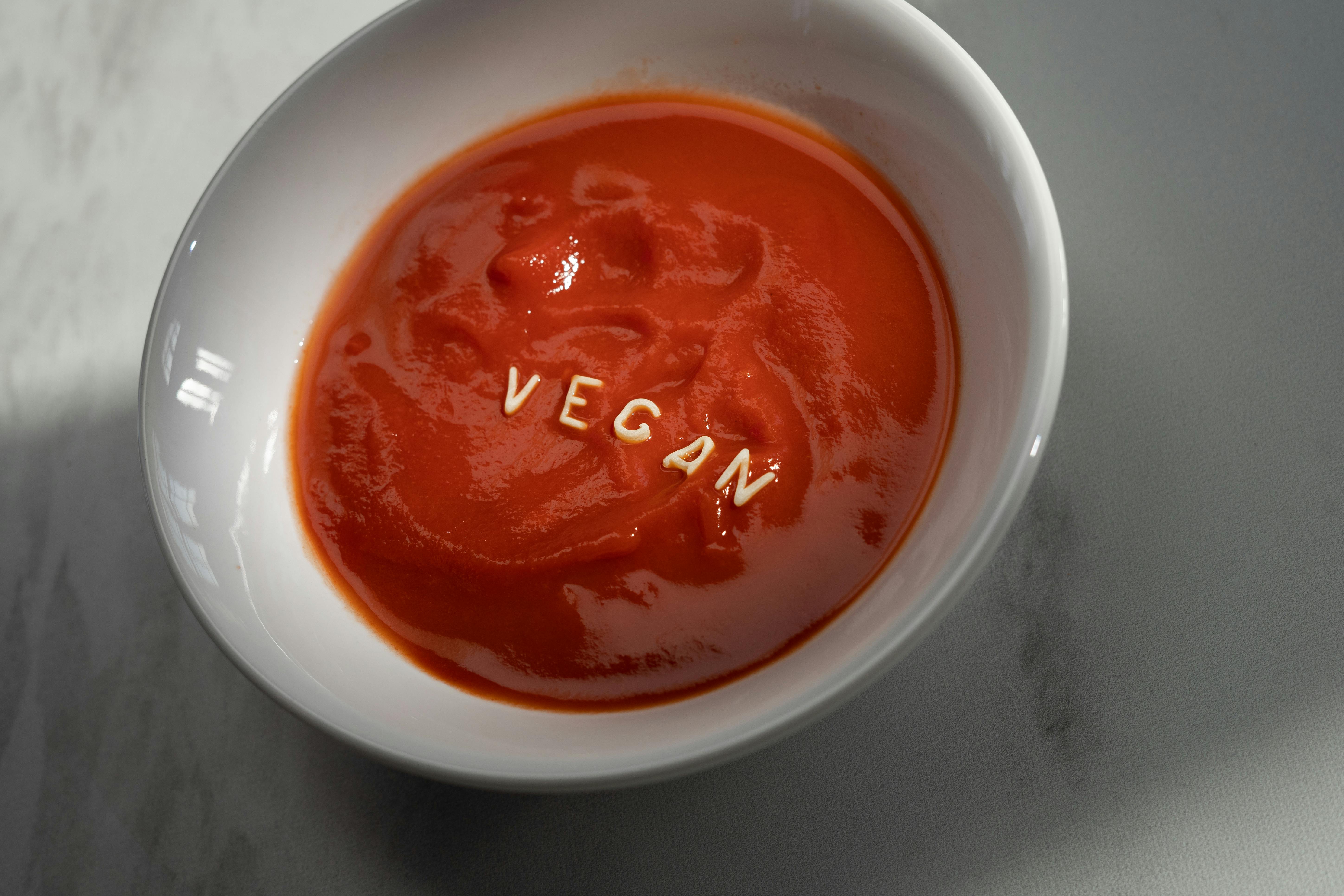 Delicious vegan tomato soup with alphabet pasta spelling 'VEGAN' in a white bowl.