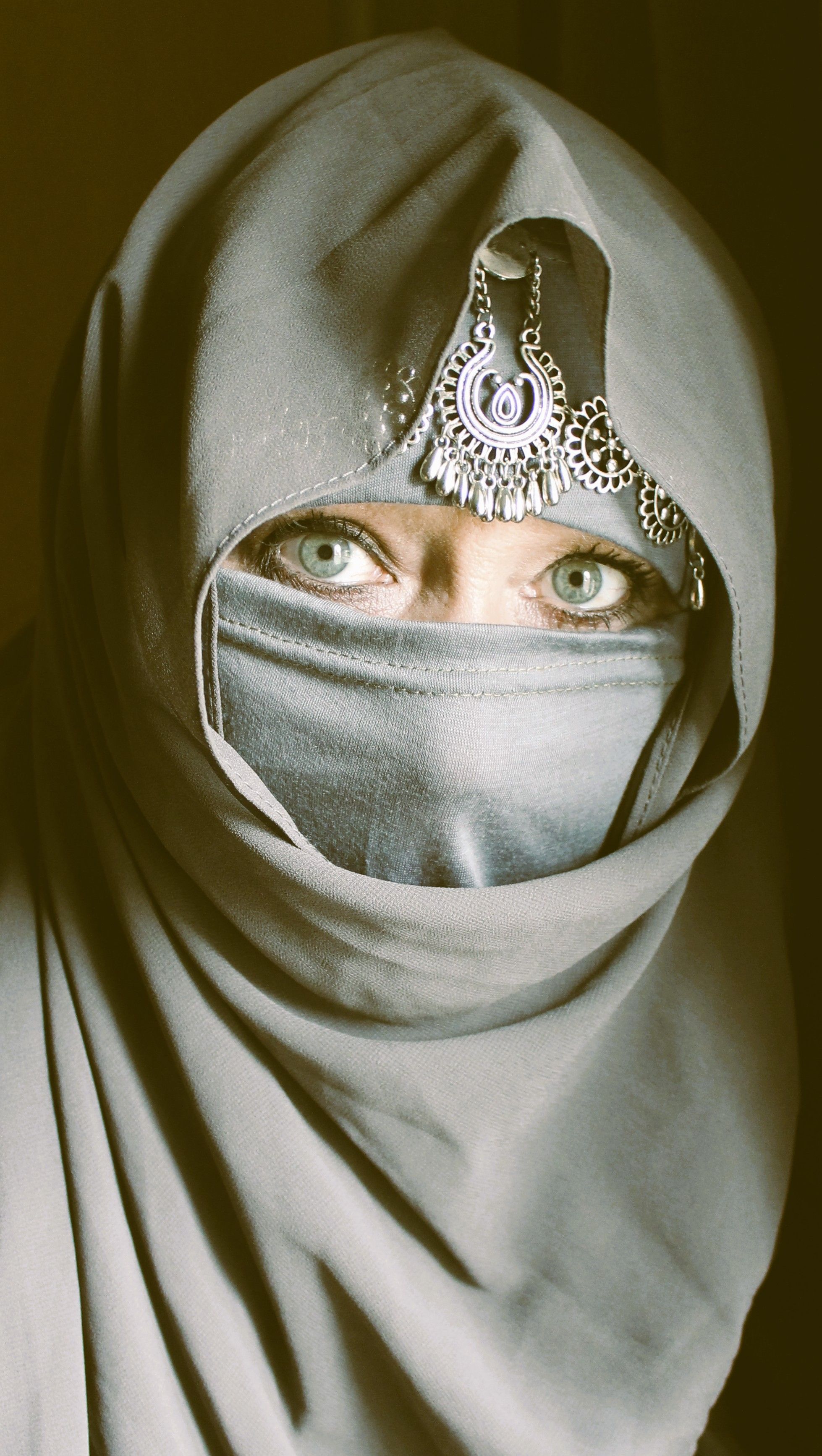 Portrait of a woman in a niqab with a captivating gaze and ornate headpiece.