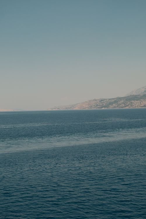 Free Serene view of a calm sea with distant mountains under a clear sky. Stock Photo