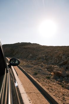 View from a car traveling on a sunlit desert mountain road.