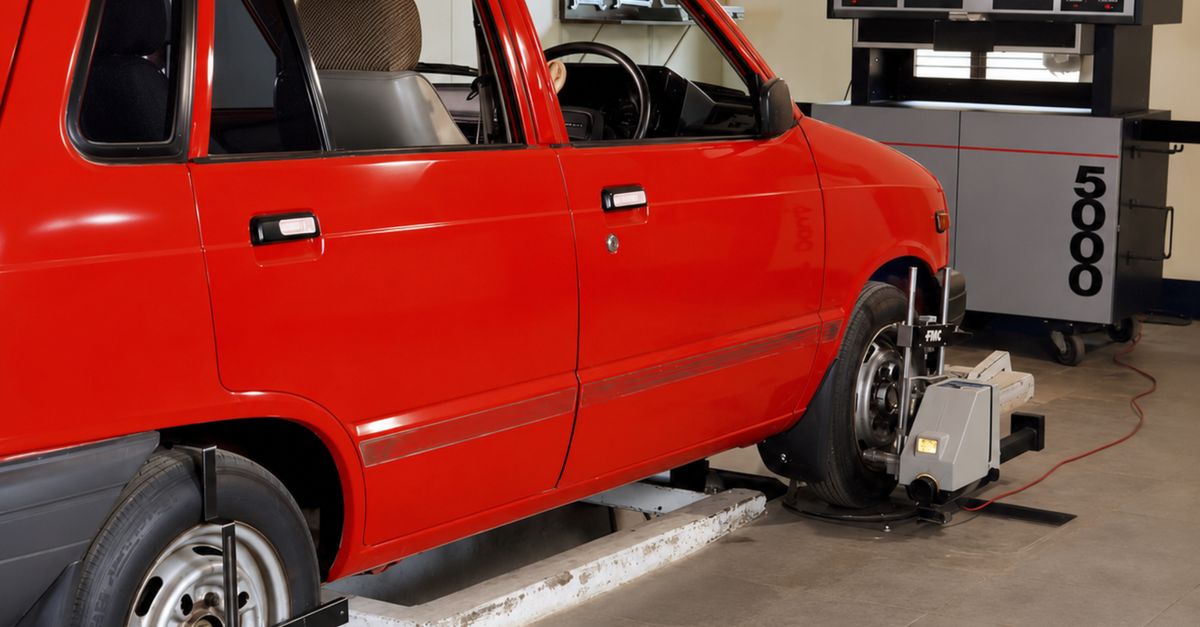 Red compact car in an automotive workshop undergoing computerized wheel alignment service.