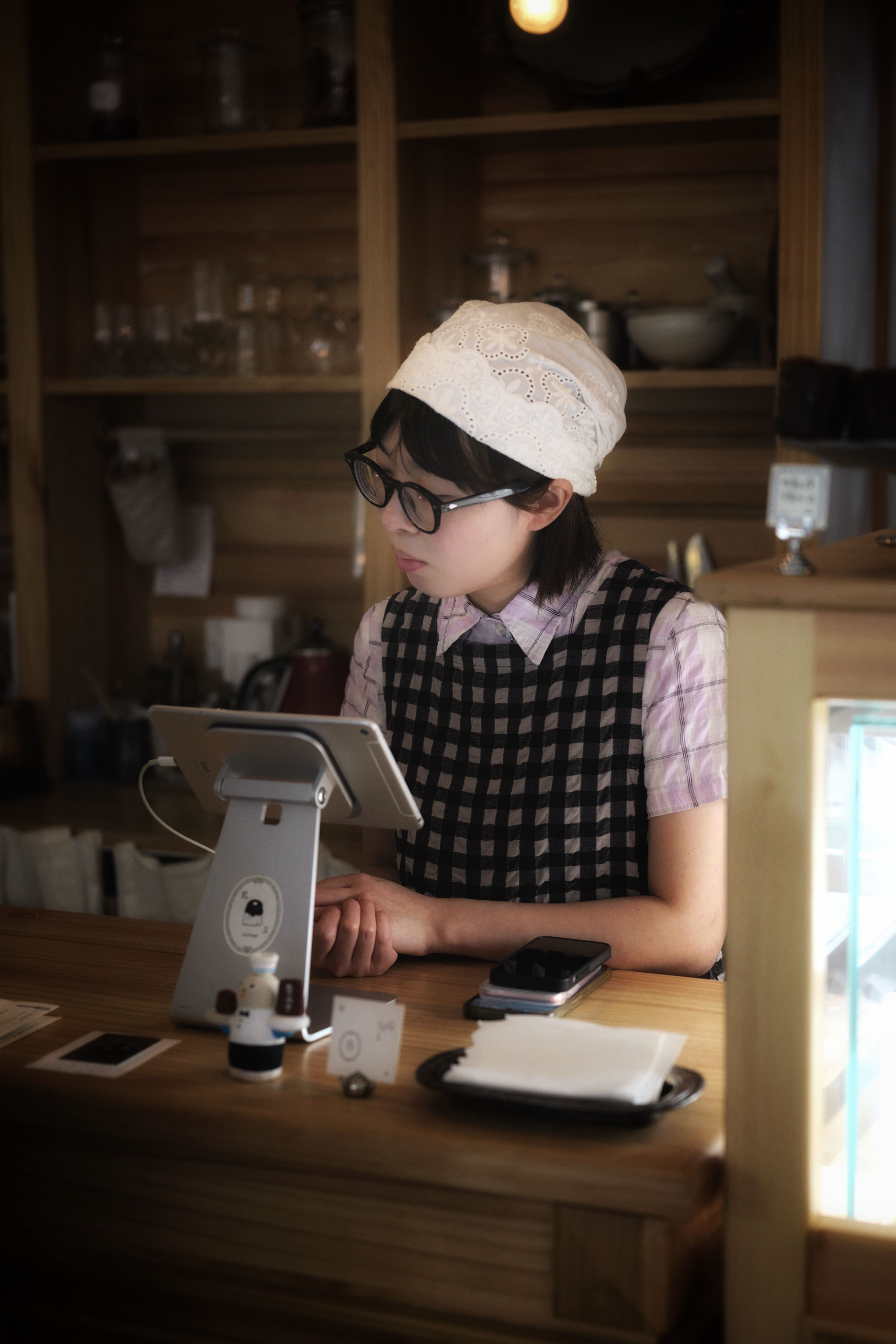 A young barista in a cozy coffee shop using a tablet at the counter