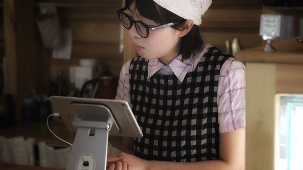 A young barista in a cozy coffee shop using a tablet at the counter