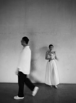 Minimalist black and white photo of a bride with a blurred figure passing by.