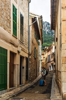A lone traveler with a suitcase walks down a narrow, picturesque street in Sóller, Mallorca.