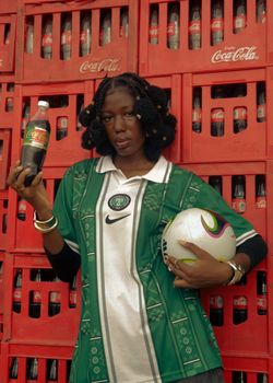 Woman in green jersey holding a football and soda bottle against Coca-Cola crate backdrop.