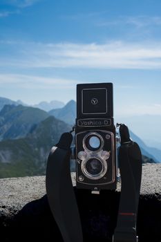 A classic Yashica-D camera set against a mountain backdrop under a clear blue sky.