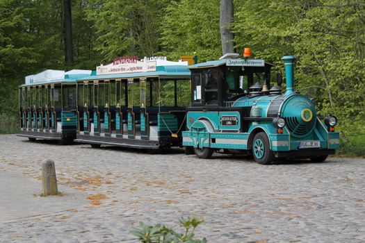 Colorful vintage tourist train parked on cobblestones in a scenic green forest.