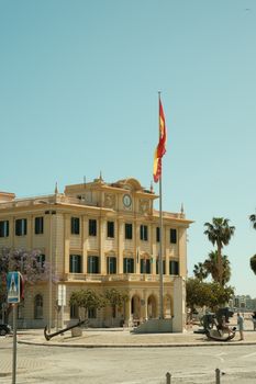 Majestic historic building with palm trees and Spanish flag in Malaga, Spain.