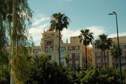 Free Scenic view of a historic building in Spain surrounded by lush palm trees under a clear blue sky. Stock Photo