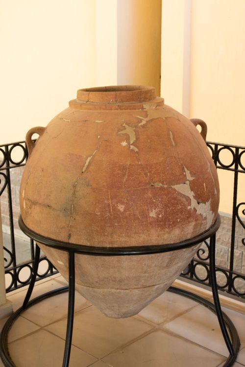 Free A large, vintage clay amphora on display in an indoor setting, surrounded by wrought iron railings. Stock Photo