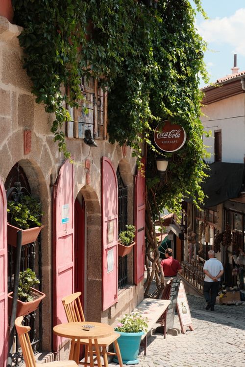 Free Charming cobblestone street with outdoor cafe and greenery on a sunny day. Stock Photo