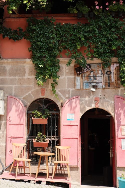 Free Rustic cafe exterior with pink shutters and greenery, inviting chairs under sunlight. Stock Photo