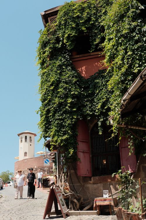 Free Charming street scene with ivy-covered building and historic tower in a sunny European town. Stock Photo