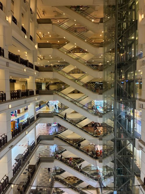 Free Interior view of a bustling multi-level shopping mall with escalators and shoppers in Kuala Lumpur. Stock Photo