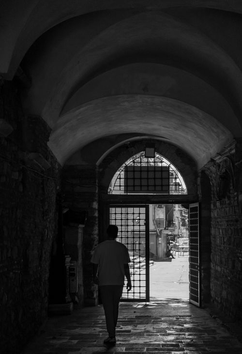 Free A lone figure walks through an ancient stone archway into daylight. Stock Photo