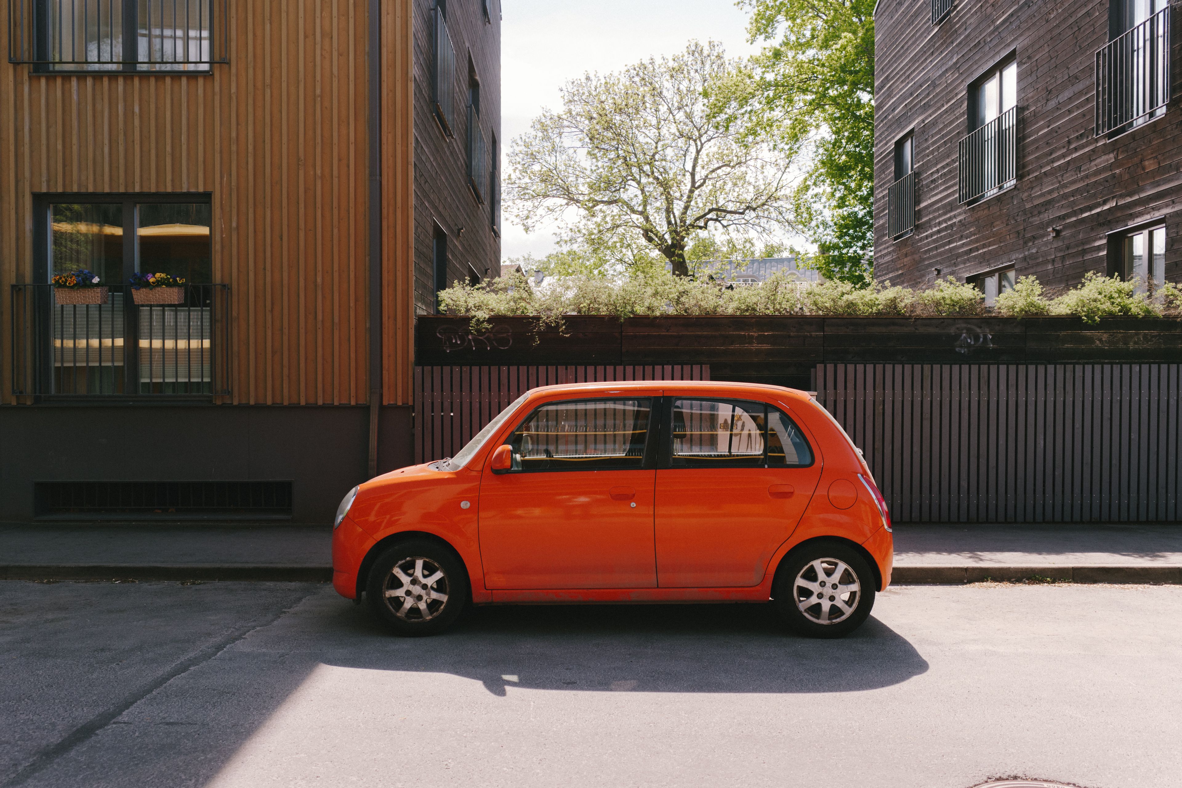 An orange car parked between wooden buildings in Tallinn, Estonia sunlight enhances the vivid color.