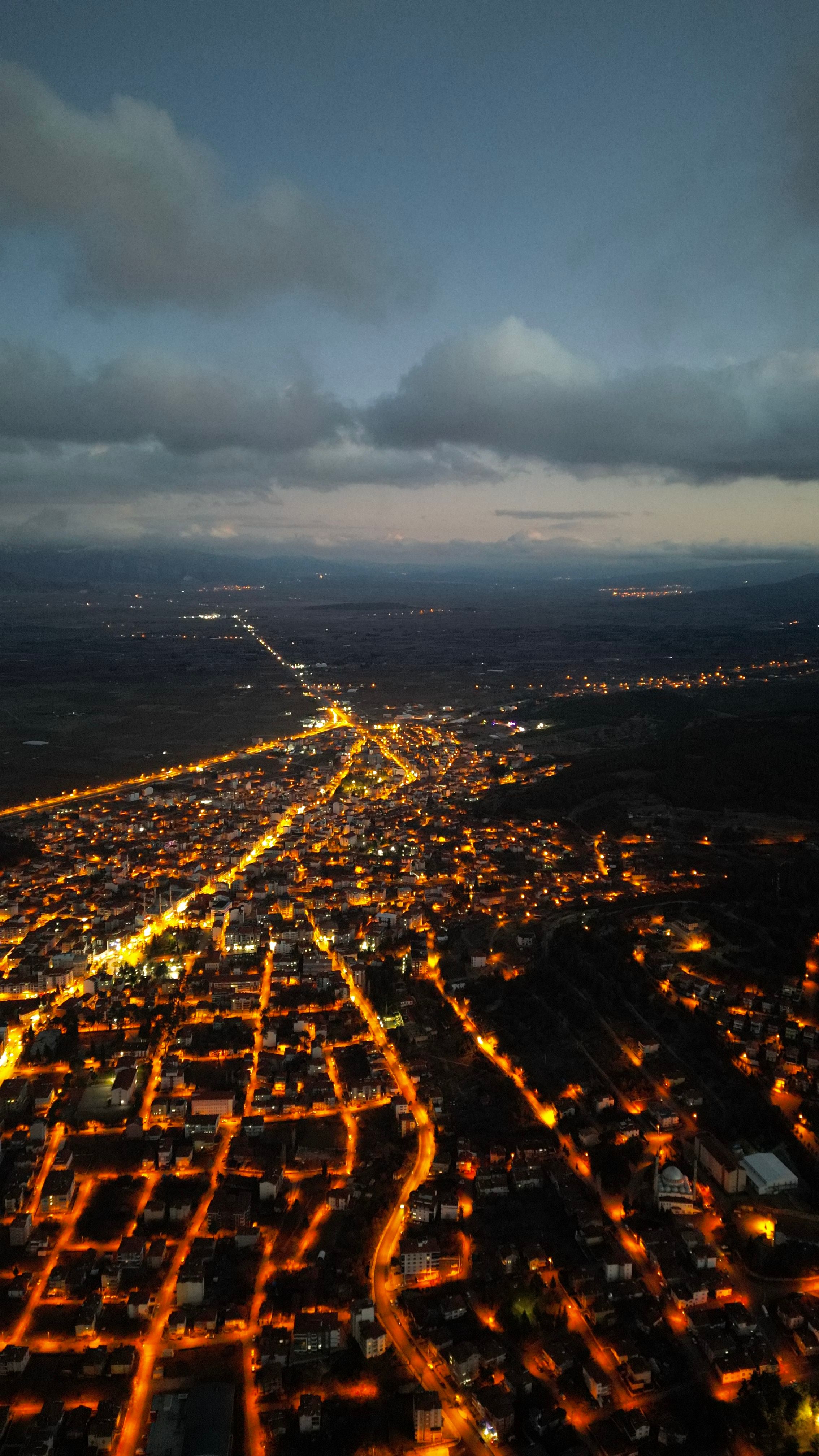 Stunning aerial night view of a Turkish town glowing with streetlights under a cloudy sky.